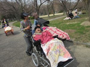 保護者さんが公園の道を車椅子の利用者さんを押して歩く写真