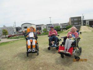 別の3人の利用者さんが芝生をバックに車椅子に乗って並んでいる様子