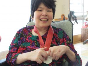 赤いひもの手作りのメダルをかけた笑顔の女性の利用者さんの様子