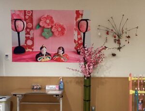 2階面会スペースの壁に飾られた桃の花やひな人形のタペストリーの写真