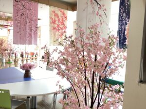 1階交流ホールに飾っている数枚の桜柄の暖簾と人の背丈ほどの桜の立ち木の造花をおさめた写真