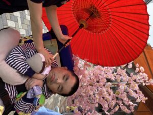 桜の立ち木飾りや和傘と一緒に外で記念撮影する利用者さんの写真２