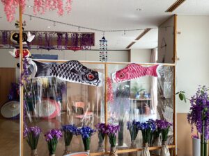 ホールの面会スペースの仕切りに飾られた外飾り用の鯉のぼりと菖蒲の花の写真