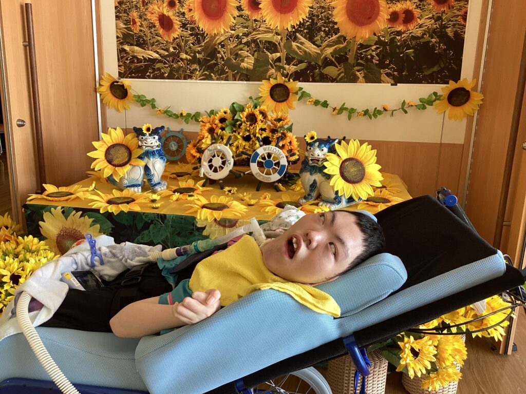 1階ホールでひまわりの飾りと一緒に写真を撮る利用者さん２