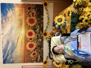 1階ホールでひまわりの飾りと一緒に写真を撮る利用者さん３